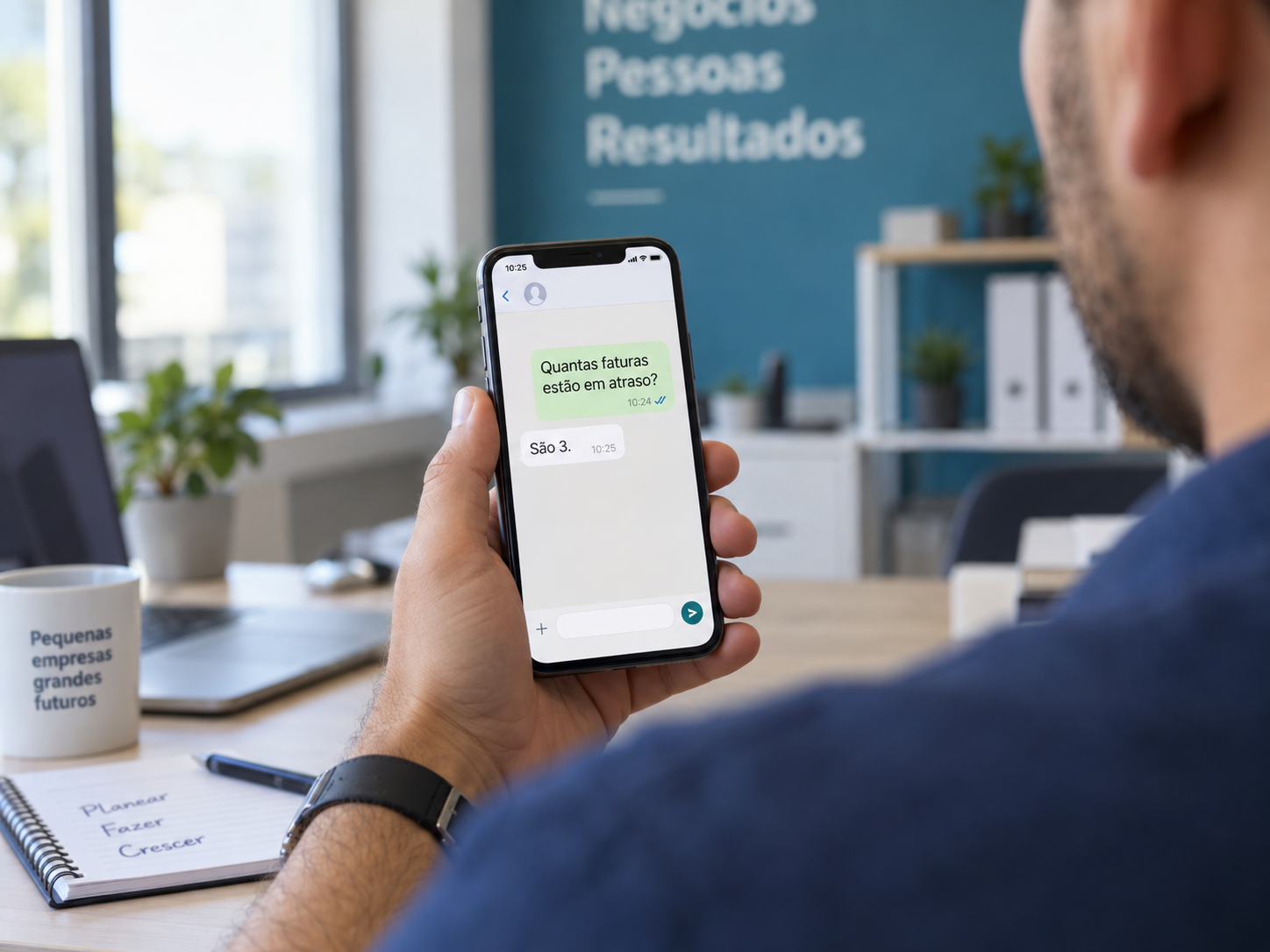 Vista por cima do ombro de alguém a ler no telemóvel uma resposta de WhatsApp com um número, num escritório luminoso